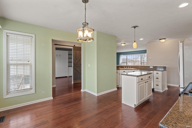 kitchen with a center island, a barn door, dark wood-type flooring, freestanding refrigerator, and a sink