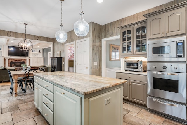 kitchen with a center island, a warming drawer, stainless steel microwave, gray cabinetry, and glass insert cabinets