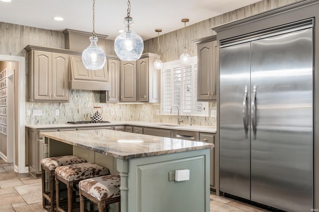 kitchen featuring a center island, custom exhaust hood, gas stovetop, a sink, and stainless steel built in refrigerator