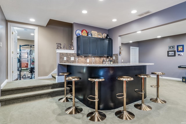 kitchen featuring blue cabinetry, a kitchen bar, visible vents, and light colored carpet