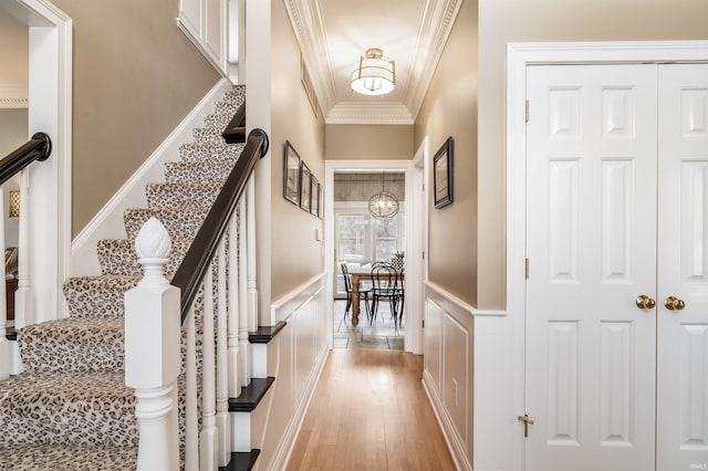 corridor featuring a wainscoted wall, light wood finished floors, a decorative wall, ornamental molding, and a chandelier