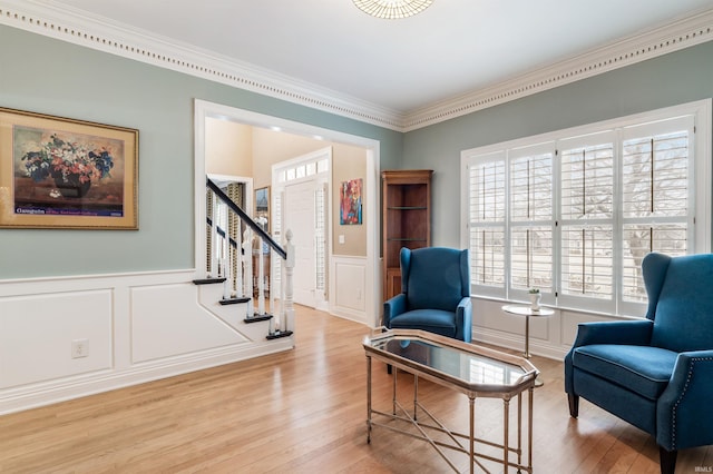 living area featuring stairway, ornamental molding, wood finished floors, and wainscoting