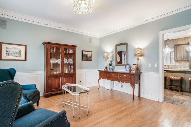 sitting room with light wood-style floors, a wainscoted wall, and crown molding