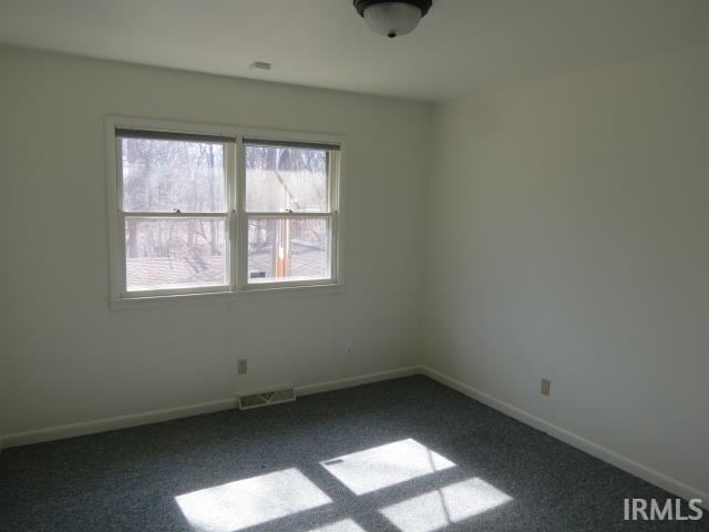 spare room featuring visible vents, dark carpet, and baseboards