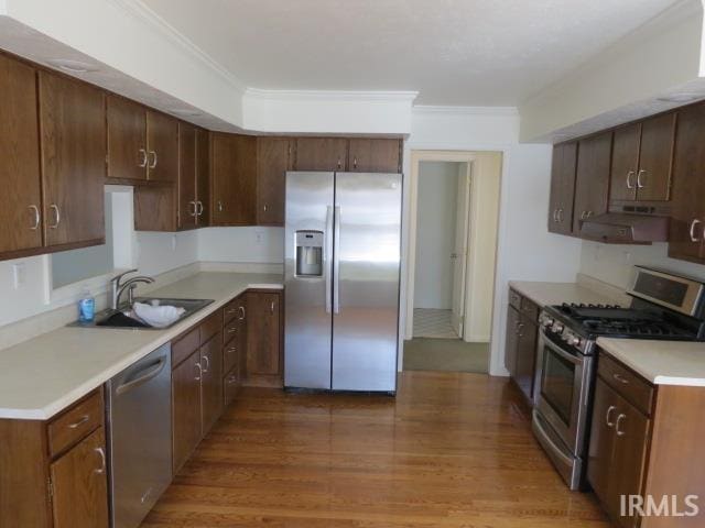 kitchen featuring under cabinet range hood, appliances with stainless steel finishes, a sink, and ornamental molding