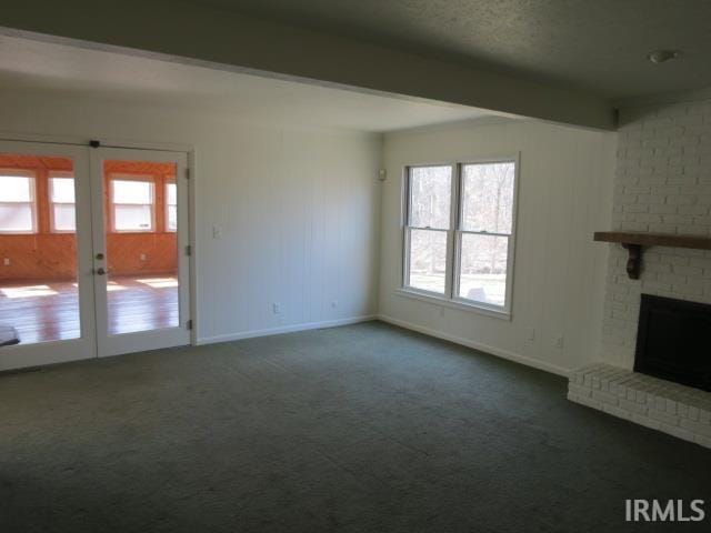 unfurnished living room with beam ceiling, dark carpet, a fireplace, and a wealth of natural light