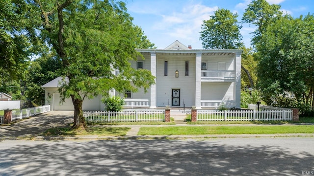 neoclassical / greek revival house featuring a balcony, driveway, a fenced front yard, and a garage