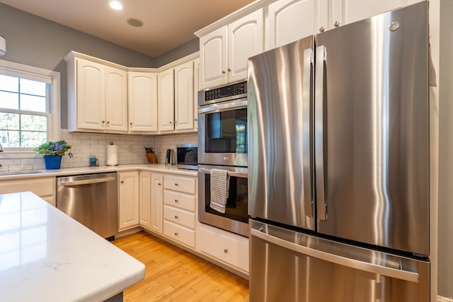 kitchen with appliances with stainless steel finishes, light wood-type flooring, recessed lighting, and tasteful backsplash