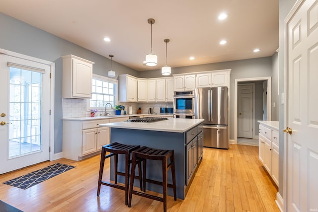 kitchen with light countertops, backsplash, appliances with stainless steel finishes, white cabinetry, and a kitchen island