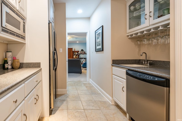 kitchen with baseboards, dark countertops, glass insert cabinets, stainless steel appliances, and a sink