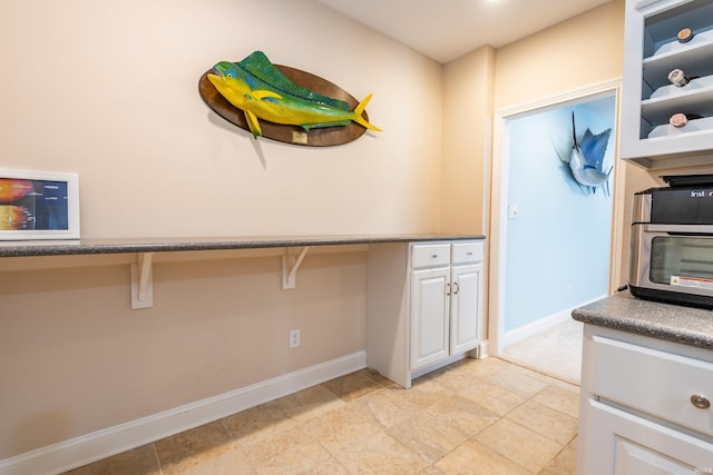 kitchen with built in desk, white cabinetry, and baseboards