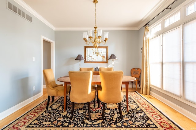 dining room featuring a chandelier, wood finished floors, visible vents, baseboards, and ornamental molding