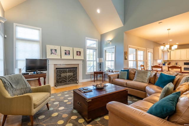 living room with high vaulted ceiling, a fireplace with flush hearth, wood finished floors, a chandelier, and baseboards