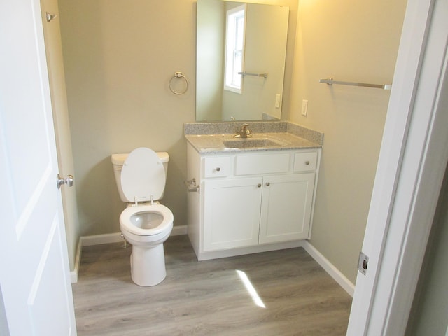 half bathroom featuring baseboards, vanity, toilet, and wood finished floors