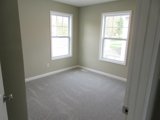 carpeted spare room featuring plenty of natural light, visible vents, and baseboards