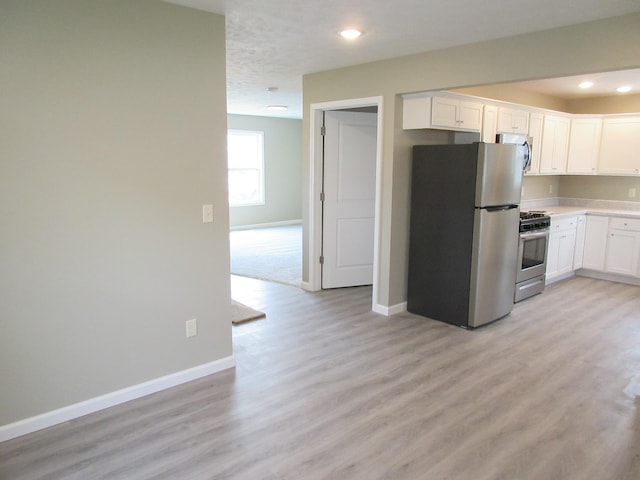 kitchen with white cabinets, light wood-style floors, baseboards, and stainless steel appliances