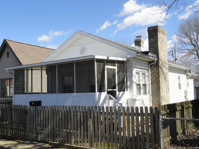 exterior space featuring roof with shingles, a fenced front yard, a chimney, and a sunroom