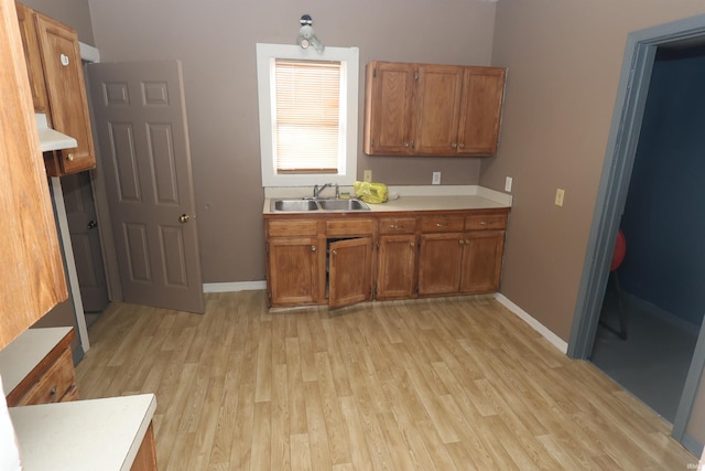 kitchen featuring a sink, baseboards, light countertops, light wood-type flooring, and brown cabinetry