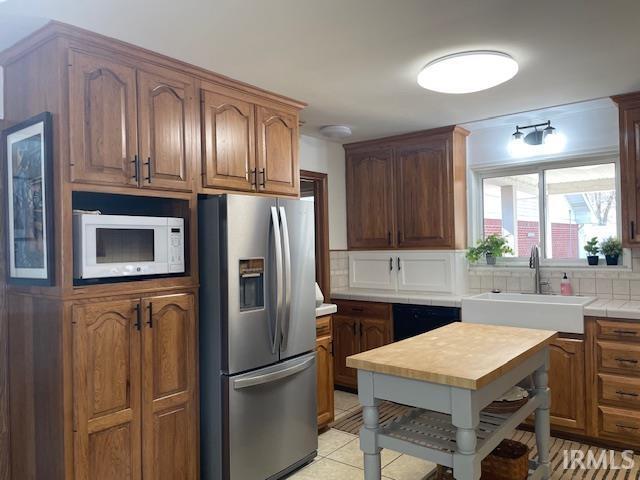 kitchen featuring light tile patterned floors, stainless steel fridge with ice dispenser, white microwave, a sink, and backsplash