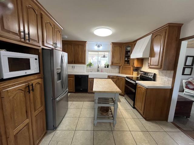 kitchen featuring light tile patterned floors, stainless steel appliances, tasteful backsplash, a sink, and wall chimney range hood