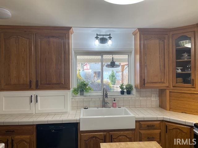 kitchen with tasteful backsplash, light countertops, glass insert cabinets, a sink, and dishwasher