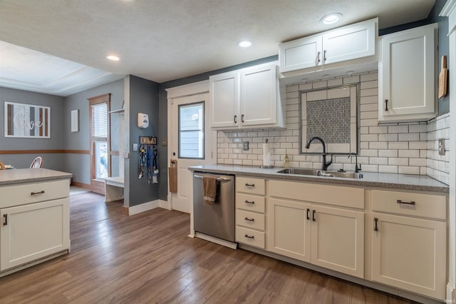 kitchen with decorative backsplash, a sink, wood finished floors, dishwasher, and baseboards