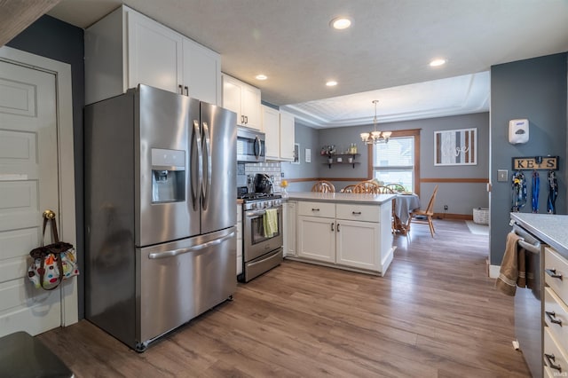 kitchen featuring a peninsula, wood finished floors, white cabinets, appliances with stainless steel finishes, and a tray ceiling