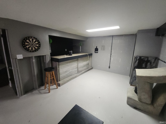 bar featuring concrete flooring, a bar, and concrete block wall