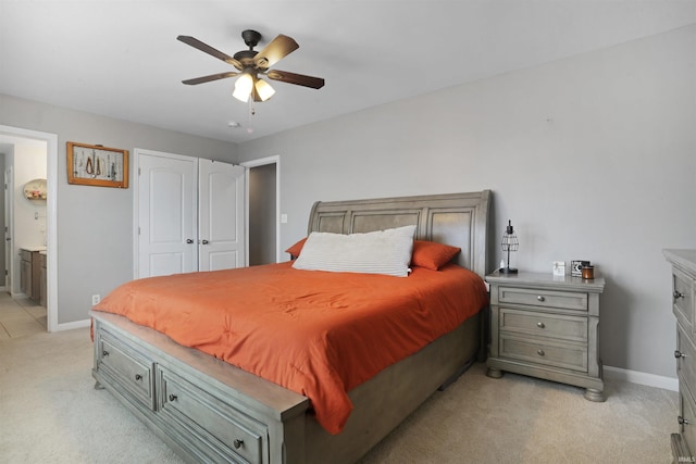 bedroom featuring light carpet, ceiling fan, baseboards, and ensuite bathroom