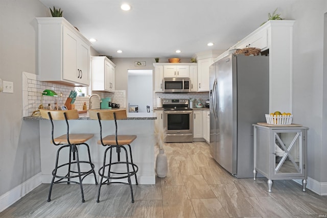 kitchen featuring appliances with stainless steel finishes, white cabinets, a peninsula, and decorative backsplash