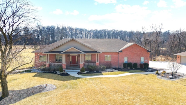 view of front of property with a porch, brick siding, a wooded view, and a front lawn