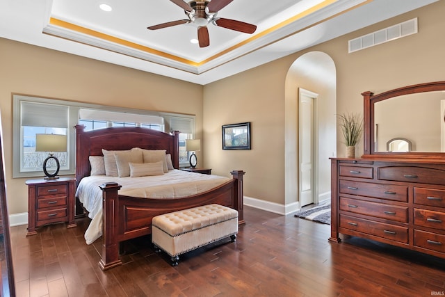 bedroom with a tray ceiling, dark wood-style flooring, visible vents, and baseboards