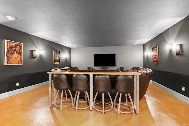 home theater room with concrete flooring, a dry bar, a textured ceiling, and baseboards