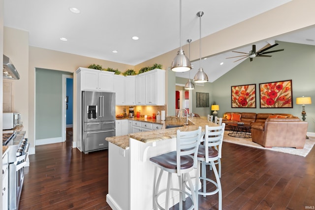 kitchen with premium appliances, a peninsula, white cabinets, open floor plan, and light stone countertops