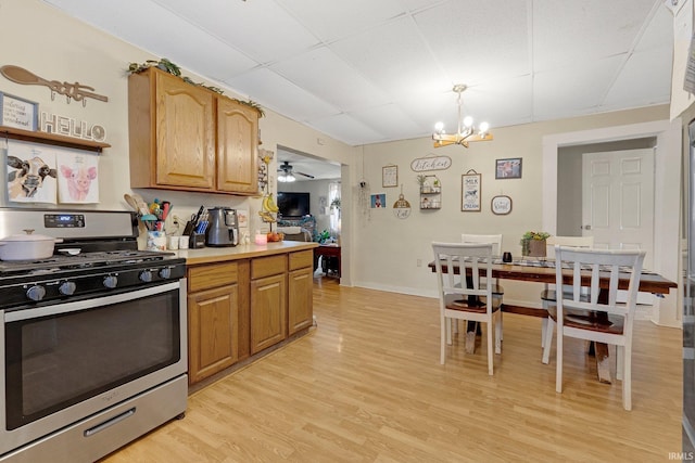 kitchen with light countertops, brown cabinetry, light wood-style floors, stainless steel gas range, and ceiling fan with notable chandelier