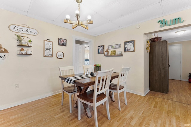 dining area featuring light wood-style flooring, baseboards, a chandelier, and a drop ceiling