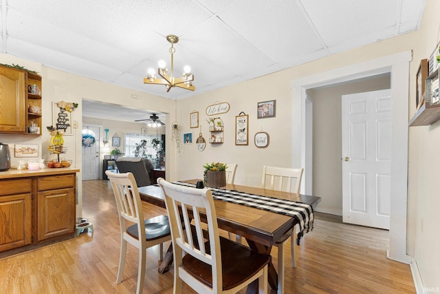 dining area featuring a paneled ceiling, light wood-style flooring, baseboards, and ceiling fan with notable chandelier