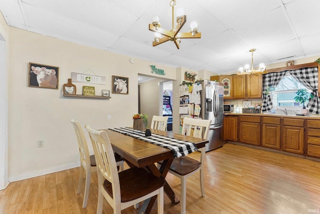 dining area featuring light wood-style flooring, baseboards, a drop ceiling, and a notable chandelier