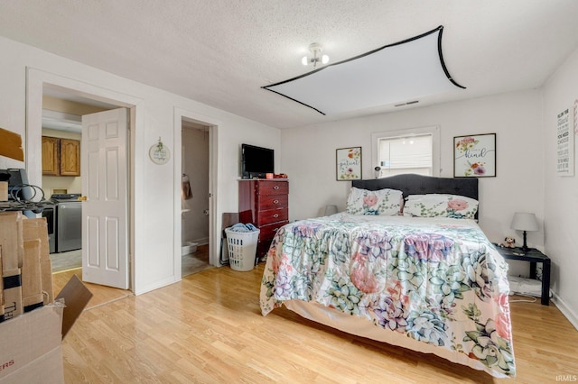 bedroom featuring a textured ceiling, visible vents, baseboards, light wood-style floors, and washer and clothes dryer