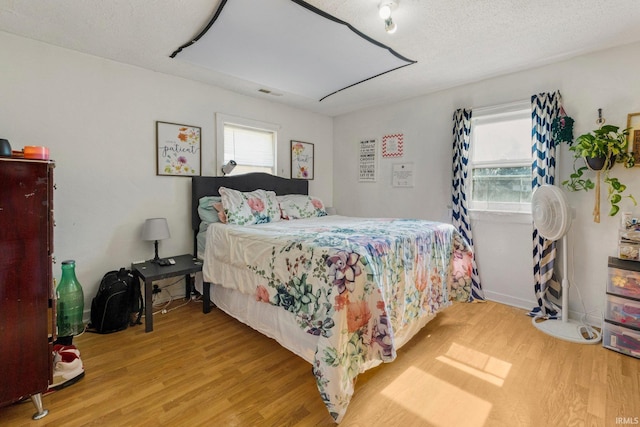 bedroom featuring light wood-style floors, visible vents, and a textured ceiling