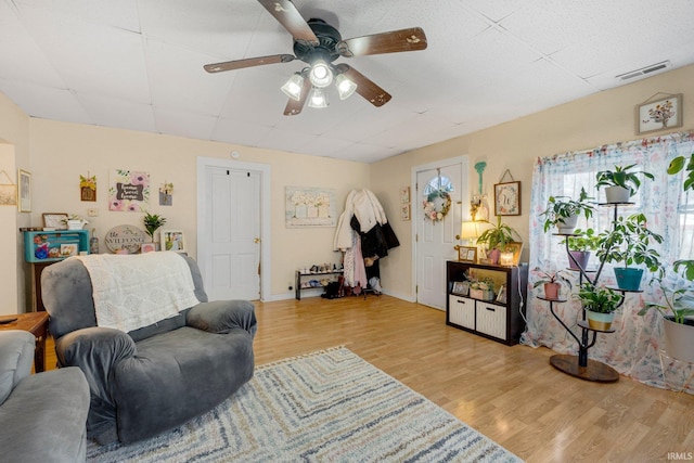 living room with light wood-style floors, baseboards, visible vents, and a ceiling fan