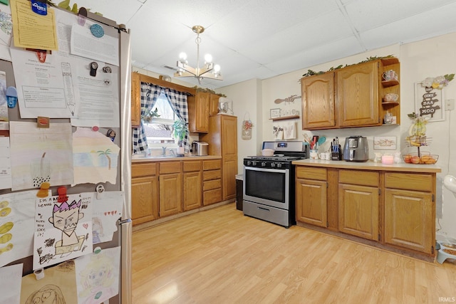 kitchen featuring light wood-style flooring, freestanding refrigerator, light countertops, stainless steel range with gas cooktop, and open shelves