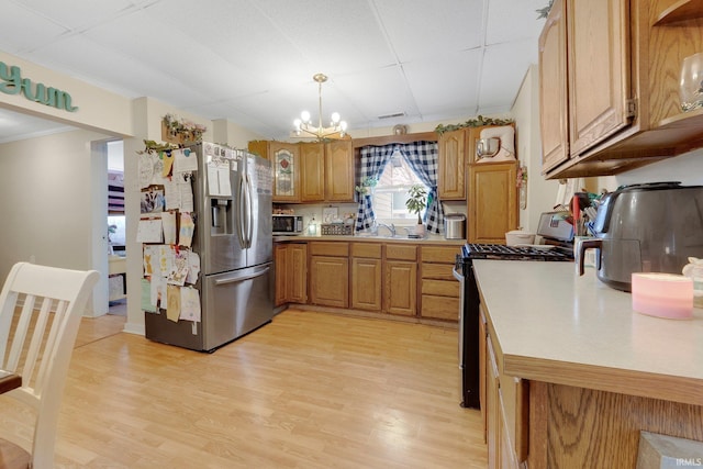 kitchen featuring a chandelier, stainless steel appliances, light countertops, light wood finished floors, and brown cabinetry