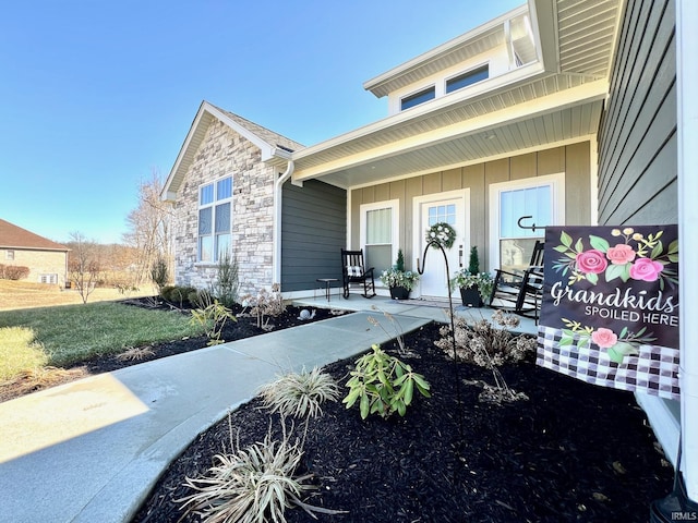 doorway to property featuring stone siding, a porch, and board and batten siding