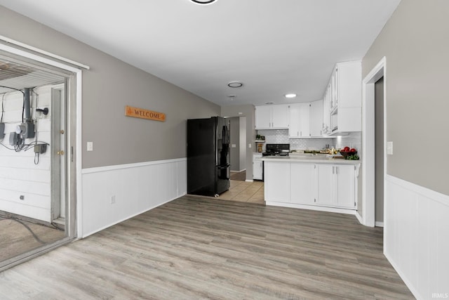 kitchen with white cabinets, wainscoting, open floor plan, freestanding refrigerator, and light wood-style floors