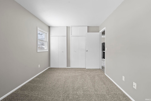 unfurnished bedroom with multiple closets, carpet flooring, and baseboards