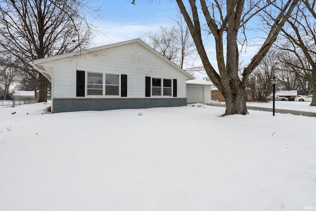 view of snowy exterior with a detached garage and brick siding