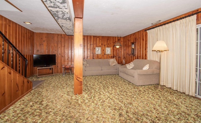 carpeted living room featuring stairway and wooden walls