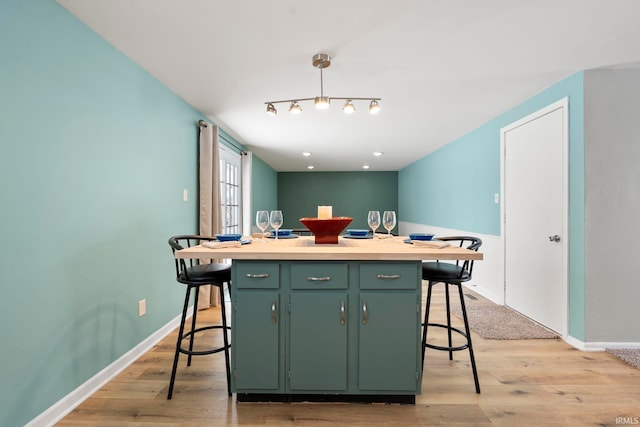 kitchen with baseboards, a kitchen island, a kitchen breakfast bar, light wood-style floors, and green cabinets