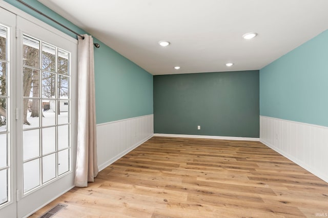 spare room with light wood-style floors, recessed lighting, a wainscoted wall, and visible vents